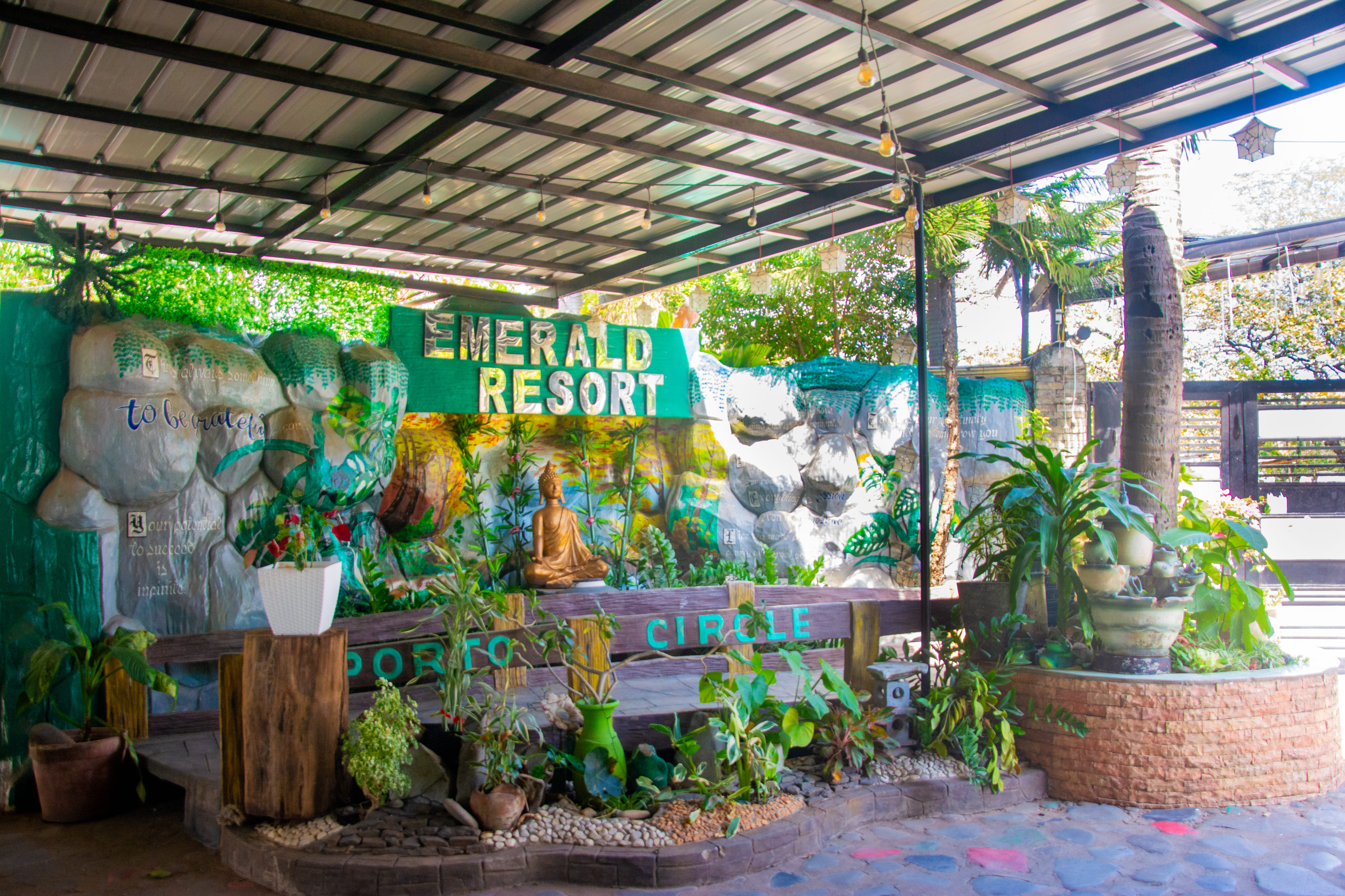 A detailed view of Emerald Resort's artistic rock wall with a Buddha statue and greenery.